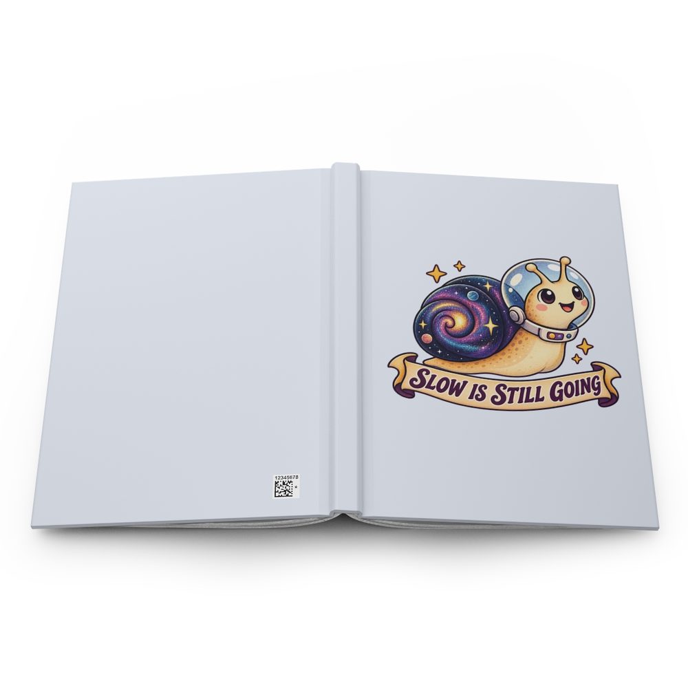 Snail Astronaut hardcover journal shown open flat, a smiling snail with a galaxy shell in a glass space helmet above a banner reading Slow Is Still Going on the front cover, with a pale blue spine and back