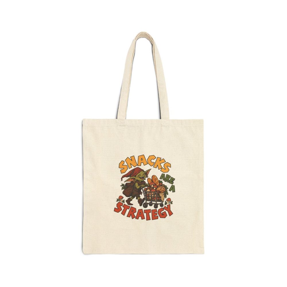 Goblin Grocery tote bag in natural cotton canvas, printed with a green goblin in a red hood pushing a cart piled with bread and groceries, with the words Snacks Are A Strategy